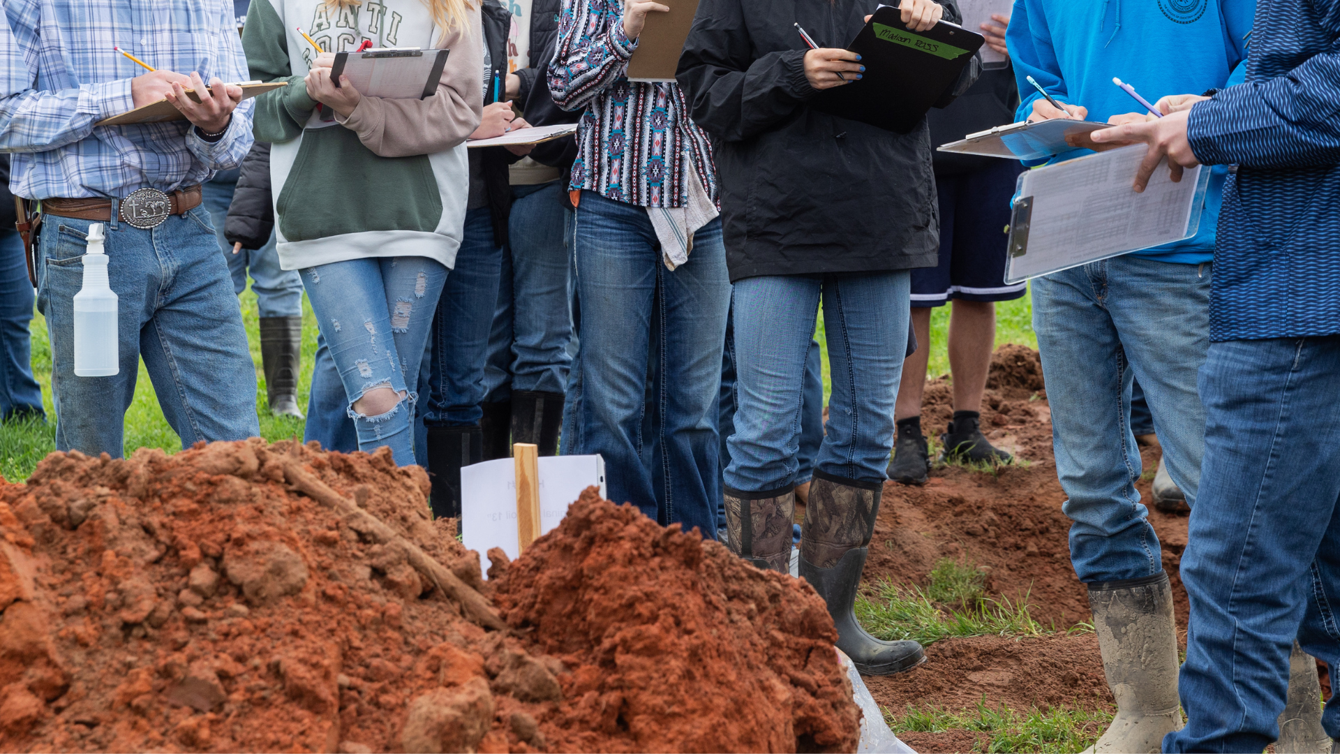 Students with clipboards examining a red dirt pile